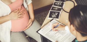 Pregnant woman at medical appointment filling in medical record with scan pictures