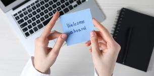 Image of a person holding a Post-It note with the word 'Welcome Aboard' written on it.