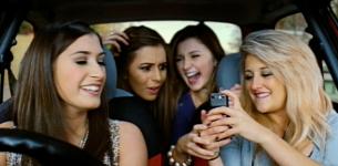 A car driver is distracted as her friends laugh about something on a mobile phone.
