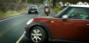A car pulls out of a side-road in front of an oncoming motorcyclist.